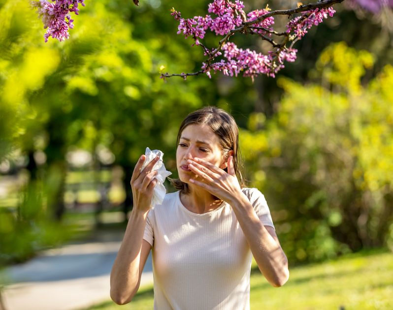 Outdoor shot of a woman with pollen allergies who feels unwell holding a piece of tissue.