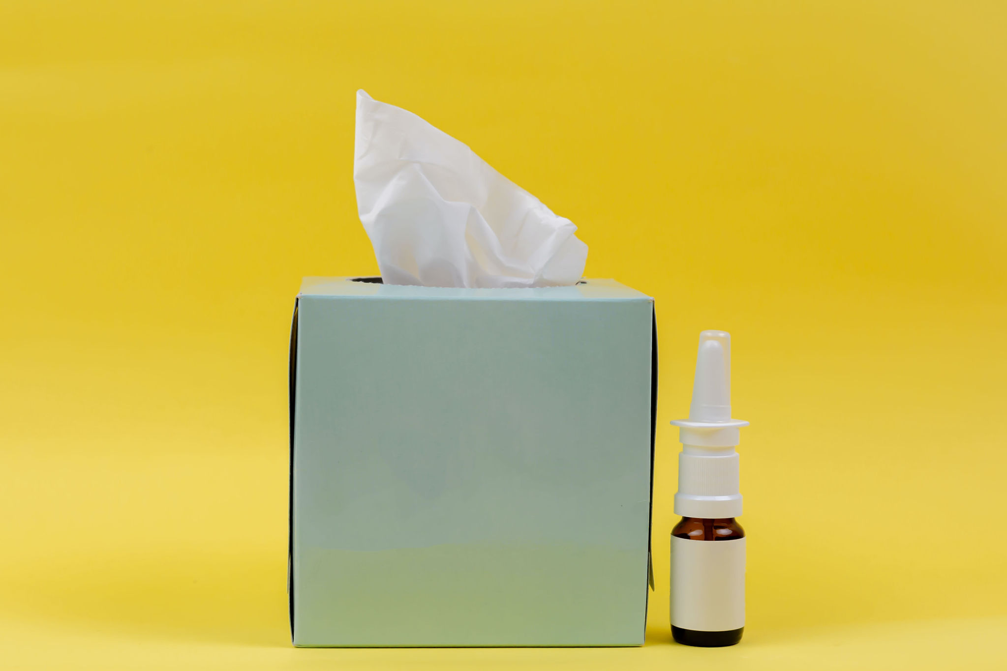 A box of tissues next to a bottle of nasal spray